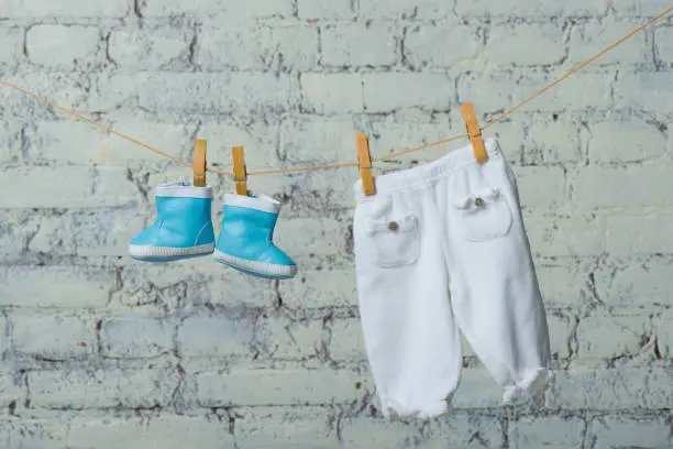 Children's boots and pantyhose dry on a rope against a white brick wall