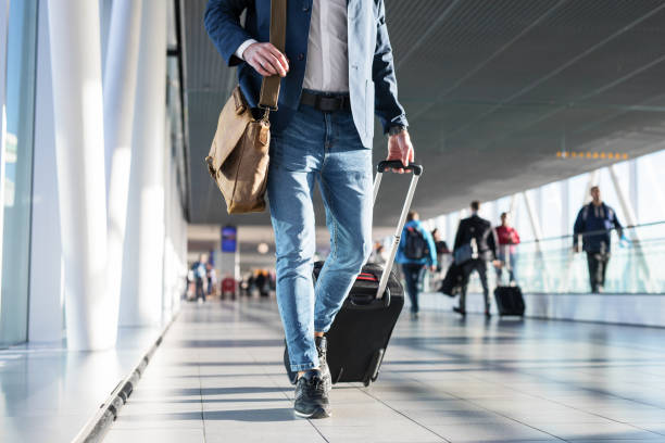 Man with shoulder bag and hand luggage walking in airport terminal Man with shoulder bag and hand luggage walking in airport terminal, photo with men's legs walking in airport terminal shoulder bag stock pictures, royalty-free photos & images