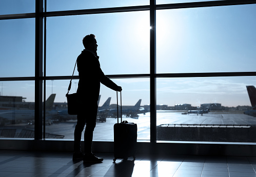 Businessman standing in airport and talking on phone, businessman silhouette against the airport terminal window