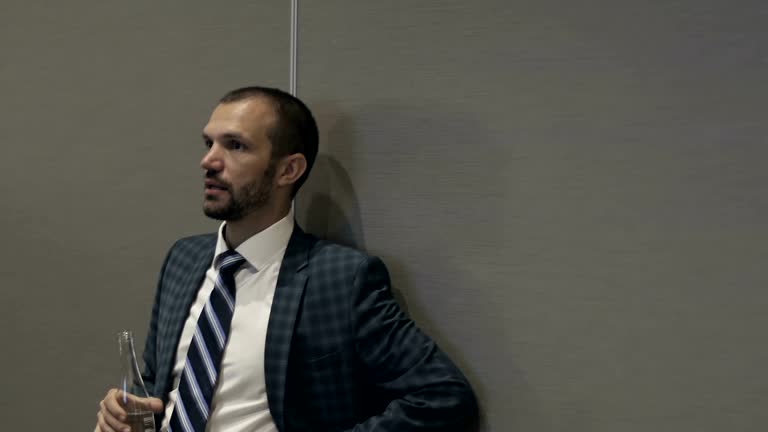 Bearded businessman drinking water from glass bottle.