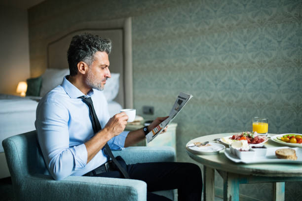 empresario maduro desayunando en una habitación de hotel. - hotel newspaper coffee reading fotografías e imágenes de stock