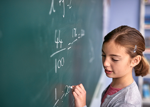 Cropped shot of an elementary school girl writing on a blackboard in class