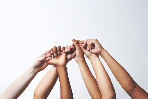 Studio shot of a group of unrecognizable people holding each others' thumbs while their hands are raised
