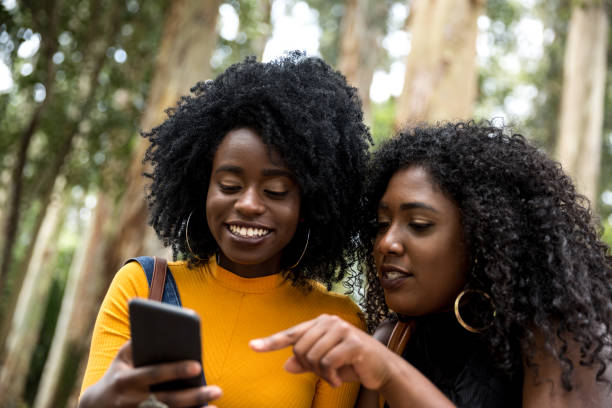 niñas de ascendencia afro con smartphone en el parque - couple black american culture african culture fotografías e imágenes de stock