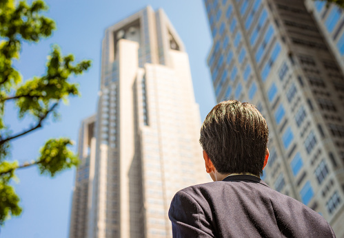 Rear view of a business man as he looks up towards the top of a tower in Tokyo's business district.