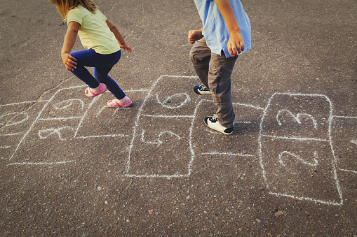 little boy and girl playing hopscotch on playground
