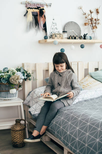 istock A little girl reads a book while sitting on the bed. 888907608