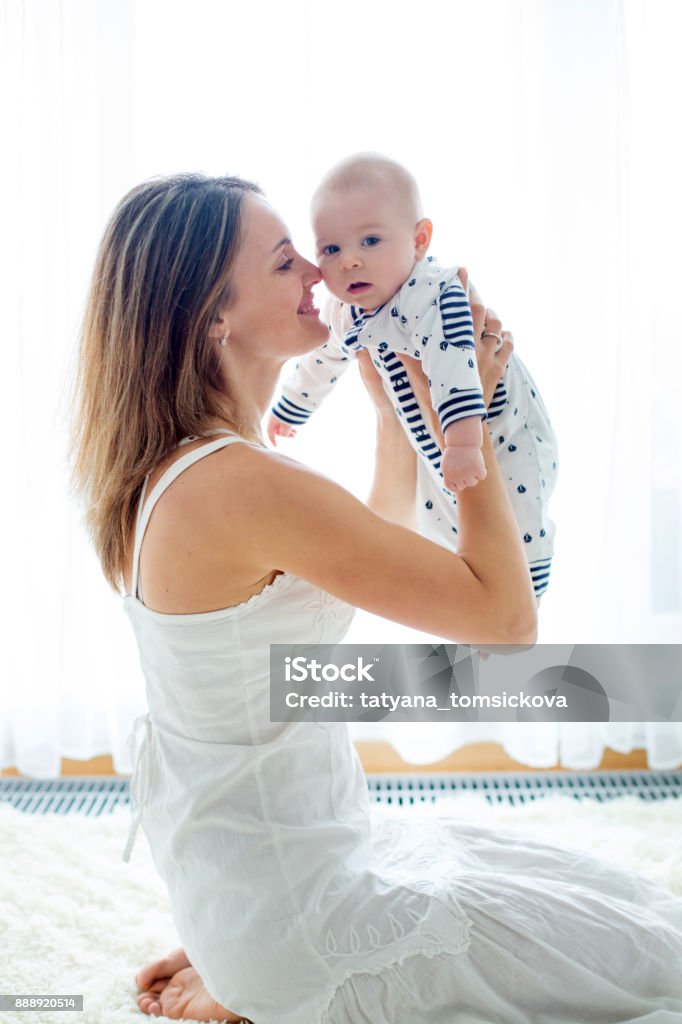 Young mother, holding her newborn baby boy at home in living room Young mother, holding her newborn baby boy at home in living room, back lit Mother Stock Photo