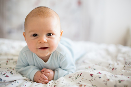 Laughing, morning and portrait of a baby on a bed to wake up, relax and play. Smile, cute and a child in the bedroom after a nap, sleeping or rest for comfort, relaxing or happiness while playing