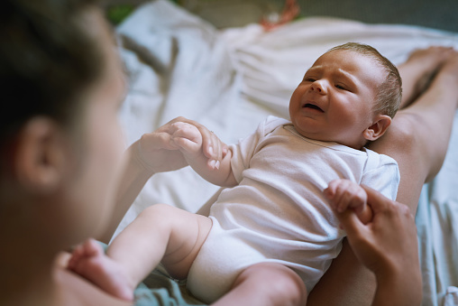 Shot of a baby boy crying as he lies in his mother’s lap at home