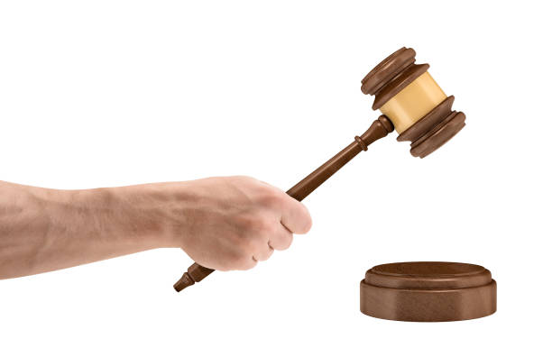 A large male hand holds a wooden judge gavel above a round sound block isolated on a white background A large male hand holds a wooden judge gavel above a round sound block isolated on a white background. Legal action. Bring to court. Business and law. arm hammer stock pictures, royalty-free photos & images