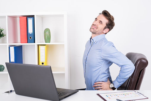 A handsome businessman is seen stretching his back at work.