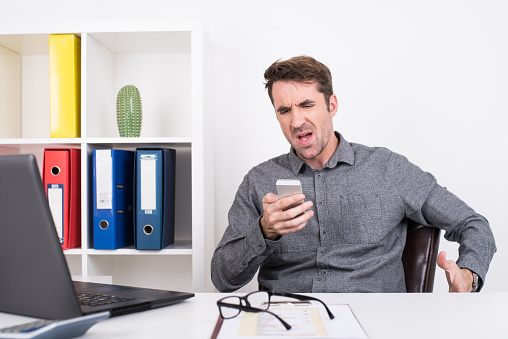 A businessman is seen angry at what he's seeing on the mobile phone.