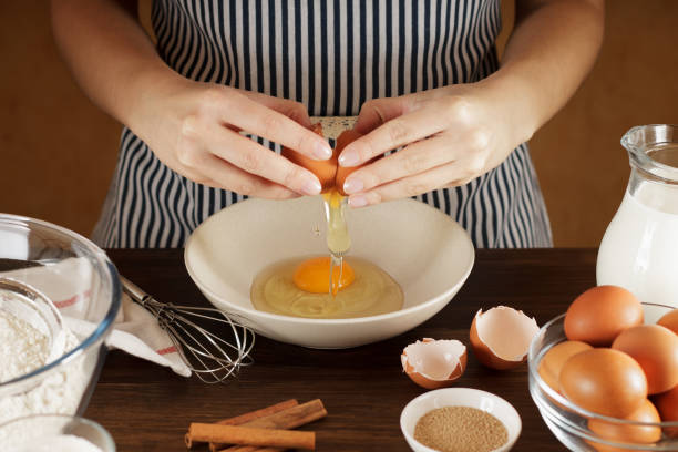 kobiece ręce wyłamujące jajko do ceramicznej miski na stole kuchennym z zastawą stołową. - breakfast bread table drop zdjęcia i obrazy z banku zdjęć