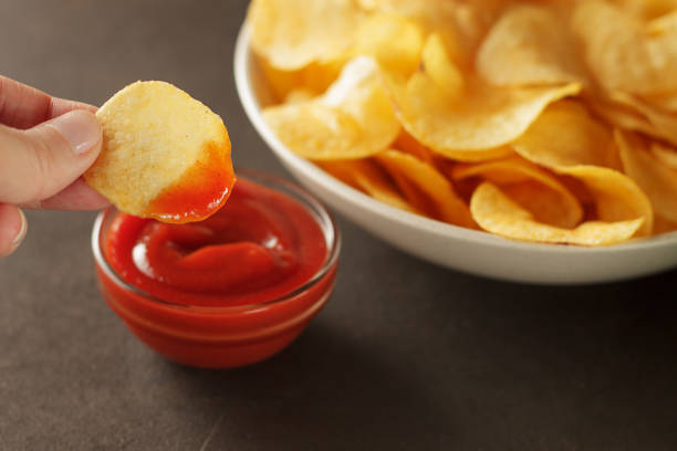 istock Hand dips potato chip into tomato sauce in glass bowl. 889025538