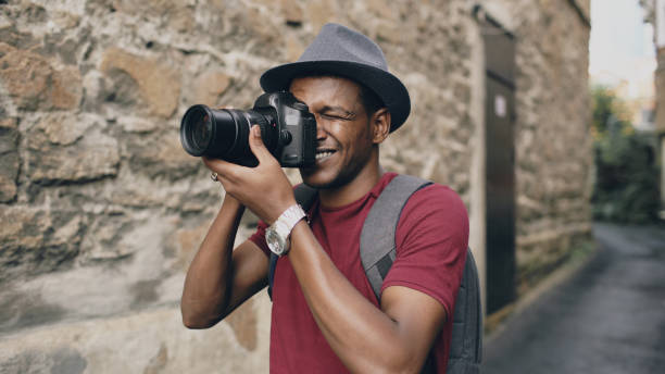 African happy tourist taking photo on his dslr camera. Young man travelling in Europe African american happy tourist taking photo on his dslr camera. Young man standing near brick wall of famous building in Europe black culture photos stock pictures, royalty-free photos & images