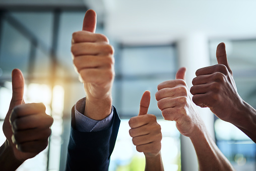 Cropped shot of a group of businesspeople giving thumbs up in a modern office