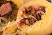 Horizontal photo of single portion of potato dumplings filled by smoked pork meat. Sour cabbage is next to meal on clay plate. Pieces of fried onion are spilled on food.
