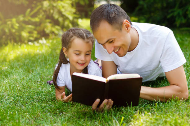 un joven padre con su hija poco lee la biblia - tree grass family human relationship family fotografías e imágenes de stock