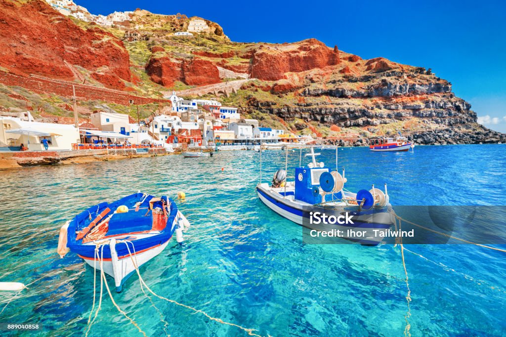 Greece. Breathtaking beautiful landscape of two fishing boats anchored to quay in fascinating blue water at the amazing old port panorama in Oia Ia village on Santorini Greek island in Aegean sea. Santorini Stock Photo