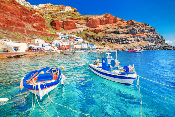 greece. breathtaking beautiful landscape of two fishing boats anchored to quay in fascinating blue water at the amazing old port panorama in oia ia village on santorini greek island in aegean sea. - caldera imagens e fotografias de stock