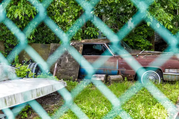 Junk car in grass behind chain link mesh fence in summer shed