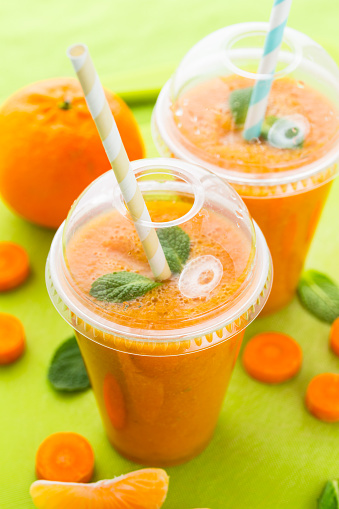 Two glasses of fresh healthy carrot orange turmeric smoothie with mint leaves