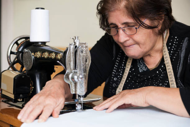 istock Senior female tailor sews on an old sewing machine 889098572