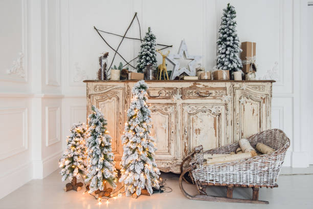 istock Christmas tree on wooden chest of drawers commode bureau in white interior, decorated with artificial flowers, garlands and toys 889108452
