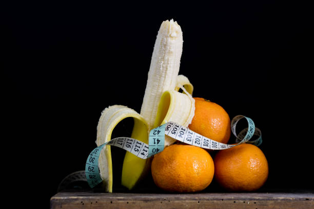 Peeled banana and measure tailor on an old kitchen table. Fruit and kitchen measure. Black background.