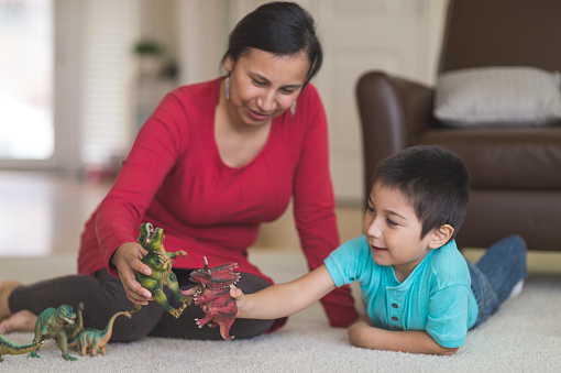 Native American mom plays with her son and toy dinosaurs on the living room floor