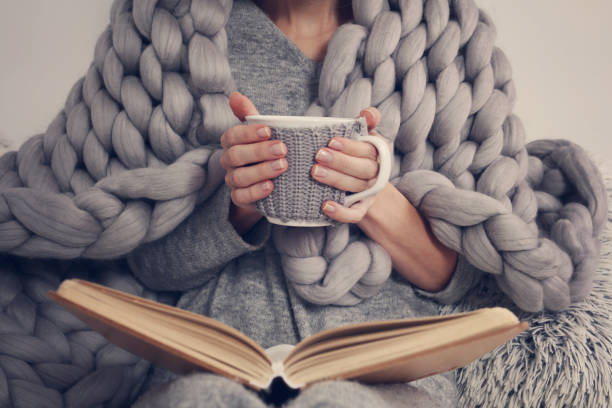 cozy donna ricoperta di calda coperta di lana merino morbido leggendo un libro. rilassati, stile di vita confortevole. - wool blanket foto e immagini stock
