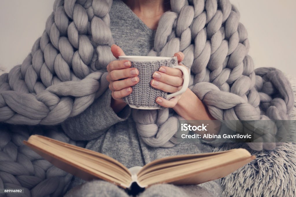 Cozy Woman covered with warm soft merino wool blanket reading a book. Relax, comfort lifestyle. Blanket Stock Photo