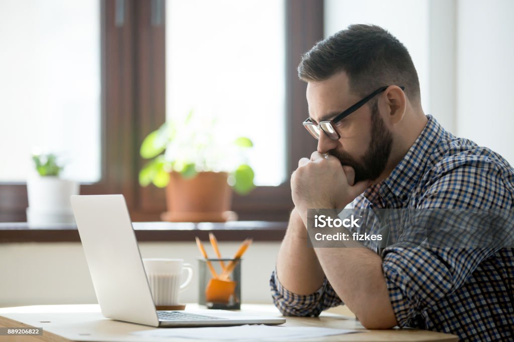 Empresario informal milenario pensando y mirando la laptop en la oficina - Foto de stock de Examen libre de derechos
