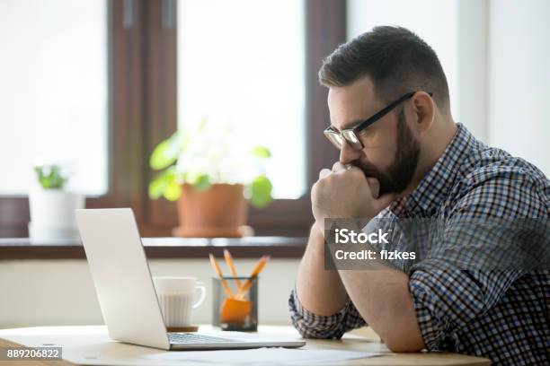 Millennial Casual Businessman Thinking And Looking At Laptop In Office Stock Photo - Download Image Now
