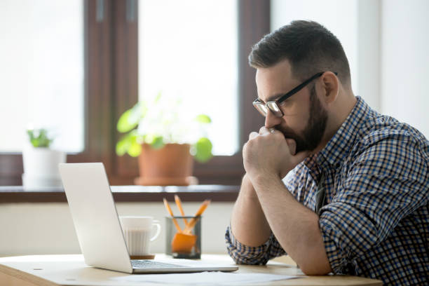 millennial casual businessman thinking and looking at laptop in office - computer thinking men people imagens e fotografias de stock