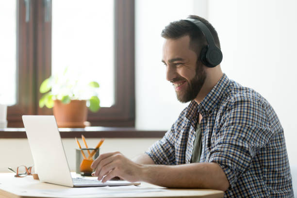 istock Smiling bearded man in headphones looking on laptop and typing 889206826