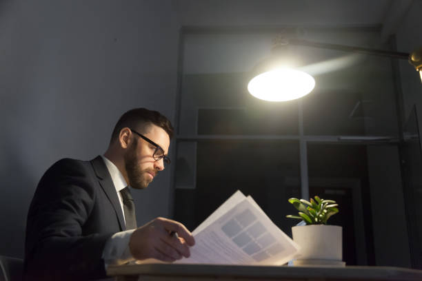 istock Concentrated bearded businessman in glasses working with documents at night 889207342