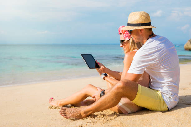 Couple using tablet on the beach Couple using tablet on the beach, idyllic photo of two hipsters using tablet computer on the beach malay couple full body stock pictures, royalty-free photos & images