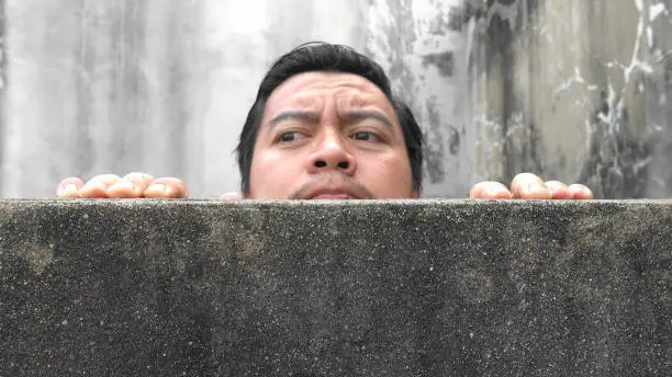 Asian men climb up concrete walls appearing suspiciously
