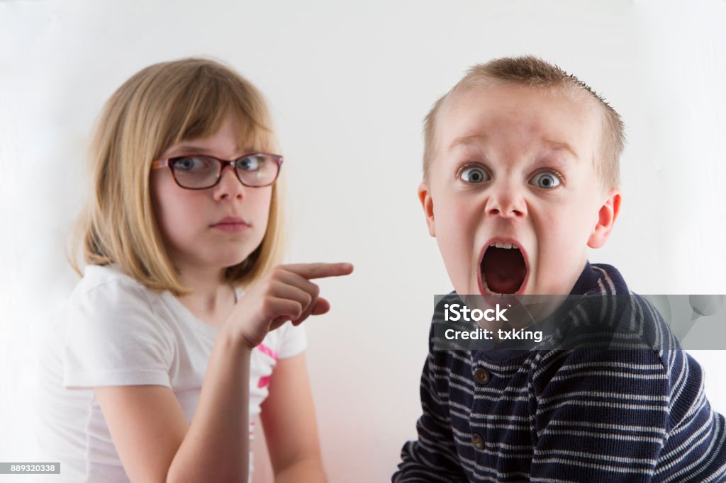 young girl pointing at a boy Boy got caught and now is in trouble and making a funny face Child Stock Photo