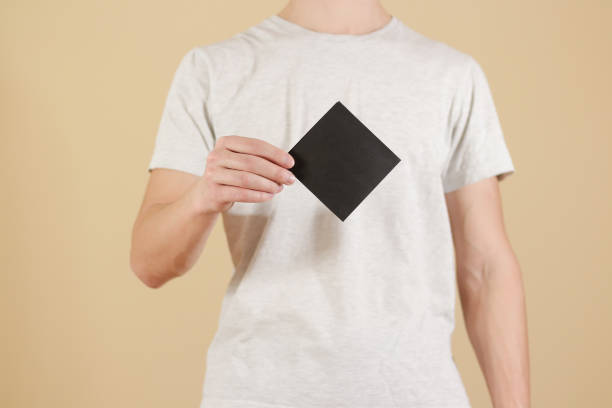 istock Man showing blank black square flyer brochure booklet. Leaflet presentation. Pamphlet hold hands. Man show clear offset paper. Sheet template. Booklet design sheet display read first person 889320650