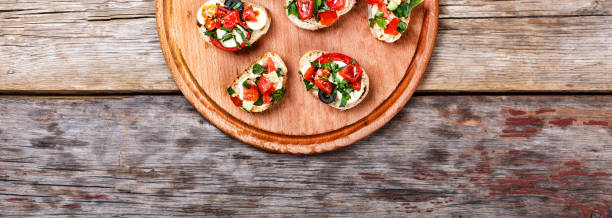 bruschetta italiana con tomates asados, queso mozzarella y hierbas sobre una tabla de cortar - bruschetta cutting board italy olive oil fotografías e imágenes de stock