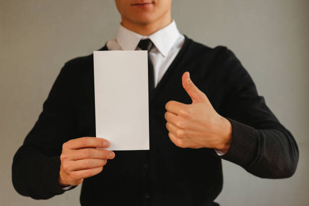 istock Business man showing blank white flyer brochure booklet and thumb up. Leaflet presentation. Pamphlet hold hands. Man show clear offset paper. Sheet template. Booklet design sheet display read first person 889362410