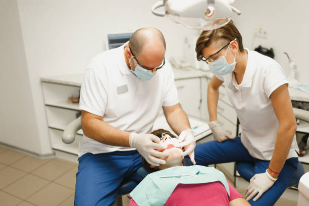 準備とセラミック クラウンをインストールするプロセス。男性プロの歯科医師と女性アシスタントは、現代のツール装備クリニック光オフィスで女性患者の歯の治療に役立ちます。 - dental light dental equipment hospital professional occupation ストックフォトと画像