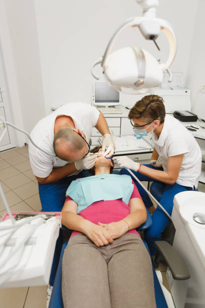 準備とセラミック クラウンをインストールするプロセス。男性プロの歯科医師と女性アシスタントは、現代のツール装備クリニック光オフィスで女性患者の歯の治療に役立ちます。 - dental light dental equipment hospital professional occupation ストックフォトと画像