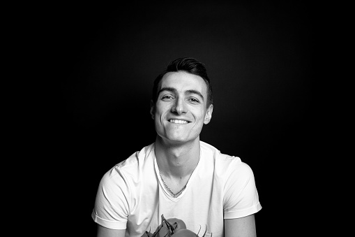 Black and white portrait of a young man in a t-shirt, smiling and looking at the camera, against plain studio background.