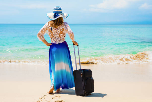 istock Woman with suitcase on the beach. 889451352