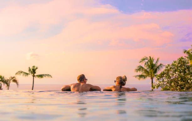 Couple looking at beautiful sunset in infinity pool Romantic couple looking at beautiful sunset in luxury infinity pool island vacation stock pictures, royalty-free photos & images