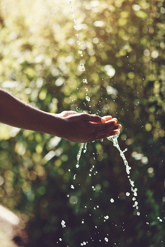 Closeup shot of a man holding his hands under a stream of water outdoors